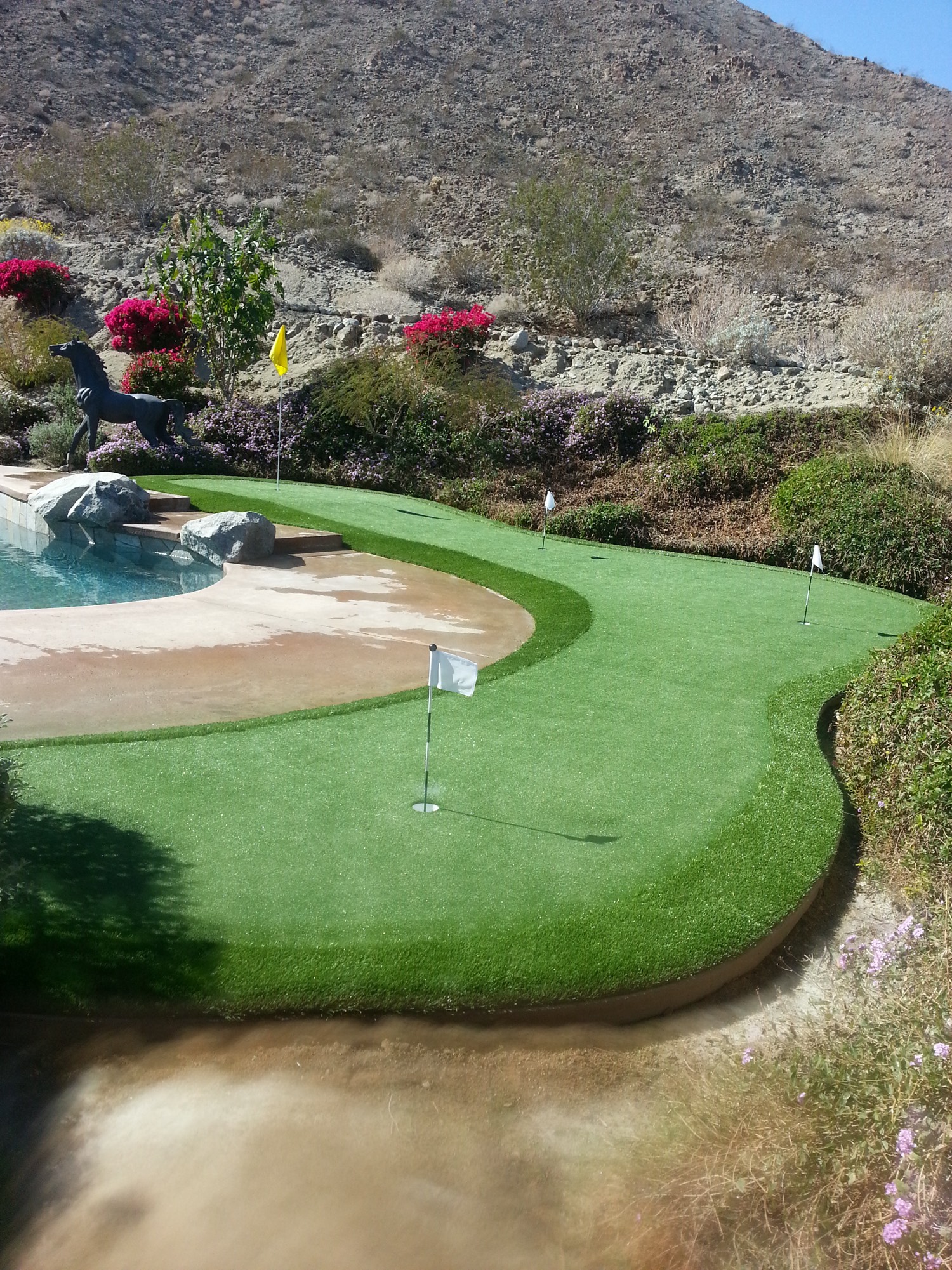 Putting green wrapping a pool, with a yellow flagstick and desert mountains beyond