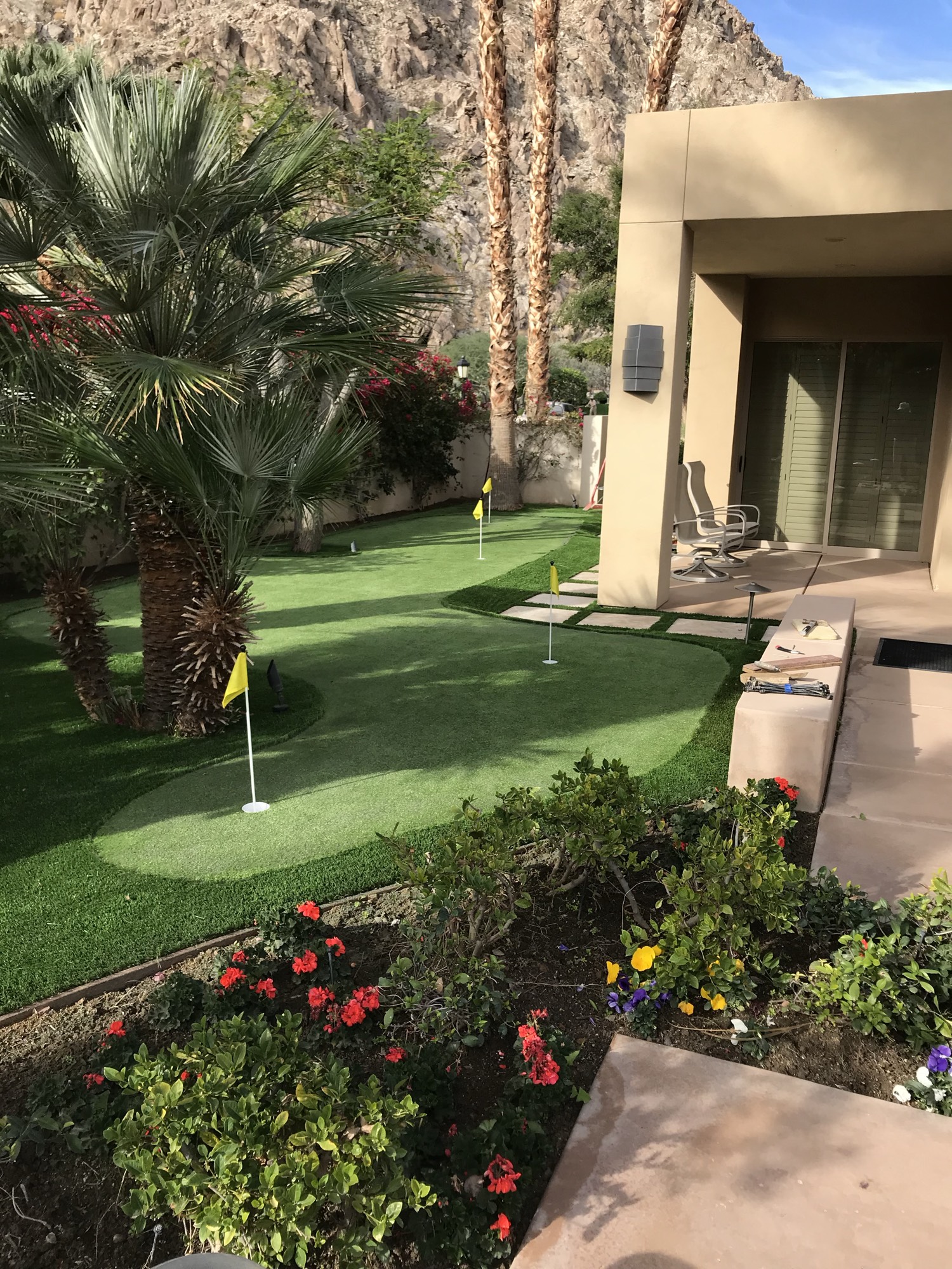 Courtyard putting green with yellow flagsticks, palms, and a desert home